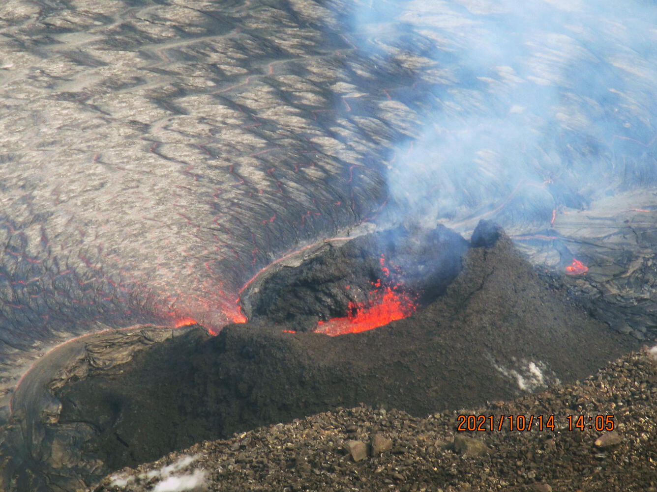 A color photo looking down at a small lava fountain surrounded by a spatter cone