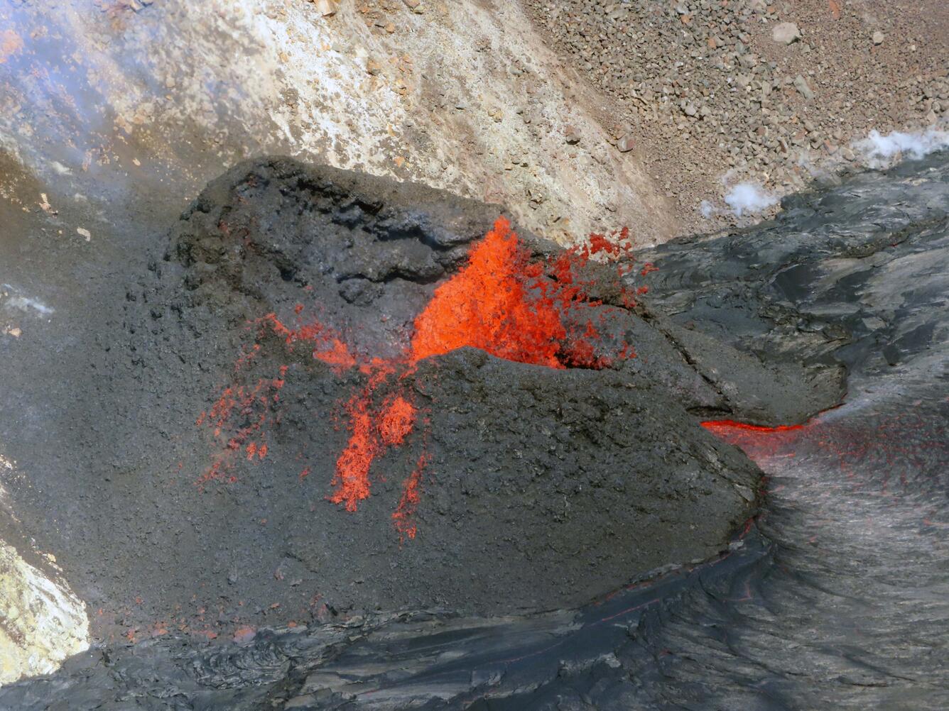 Color photo of a lava fountain depositing molten spatter onto a dark spatter cone