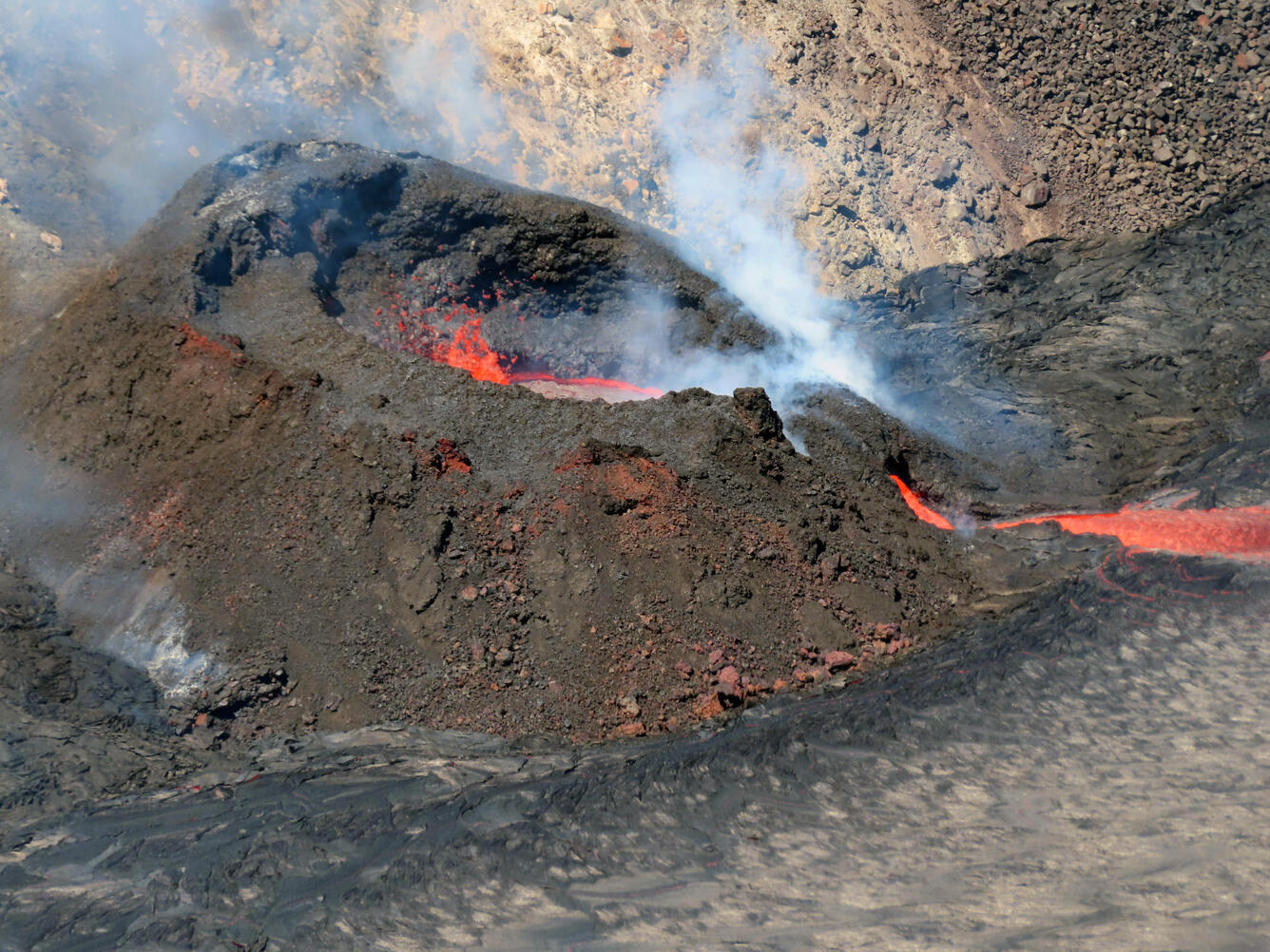 A color photo of lava fountains within a spatter cone and a small lava channel entering into a lava lake