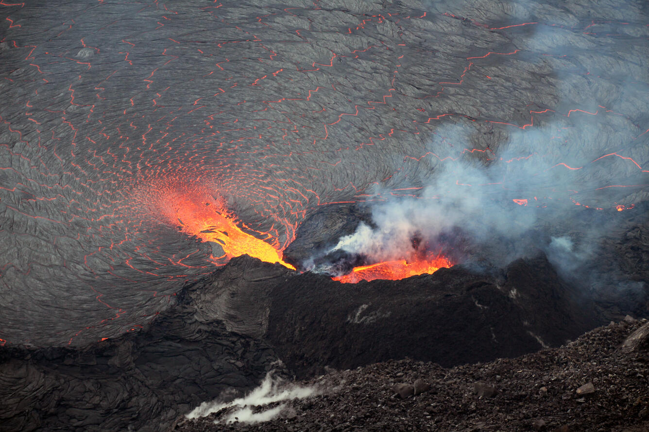 Color photograph of orange ponded lava inside of a spatter cone that is pouring into an active lava lake