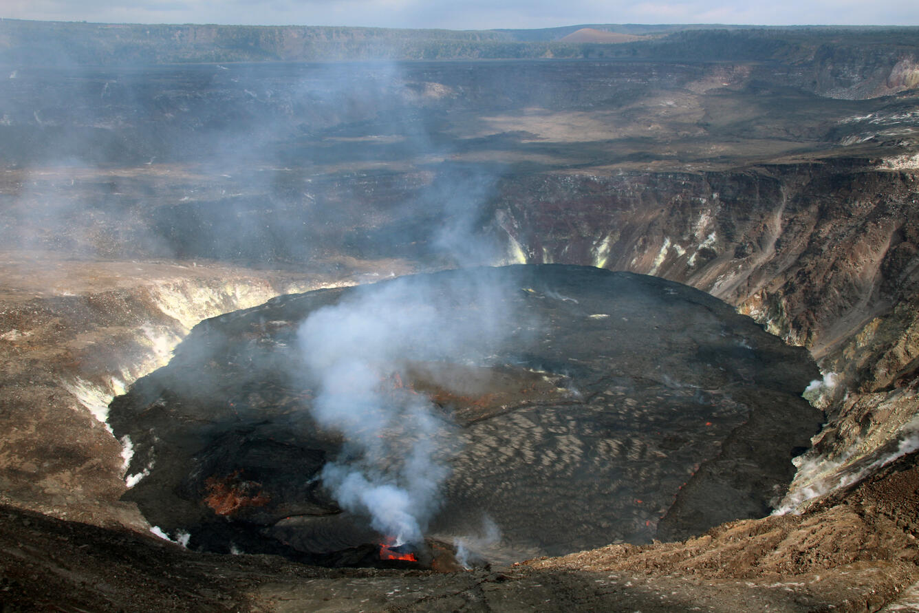 A wide view of a lava lake with a crater wall vent producing a white volcanic gas plume