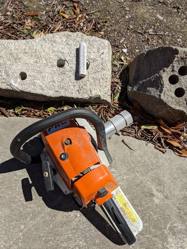 Several blocks of igneous rock are pierced swiss-cheese-style by round drill holes. The culprit chainsaw-size drill rests nearby