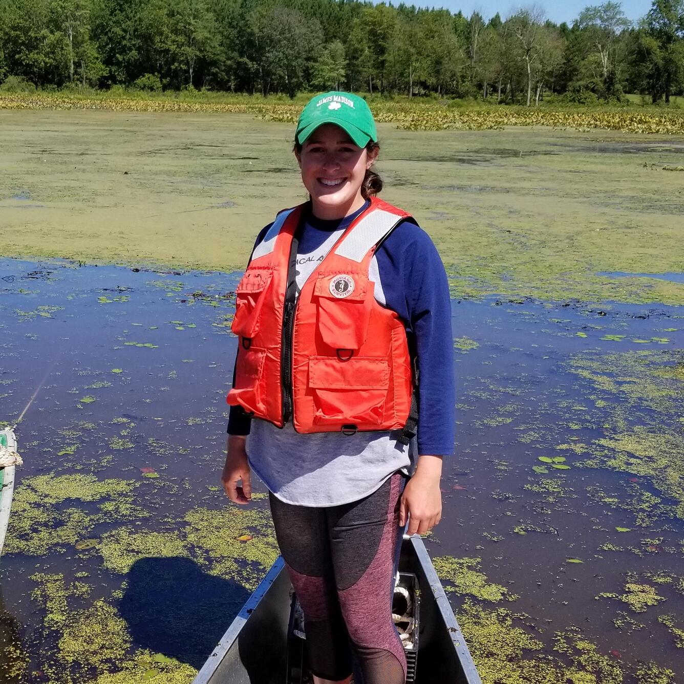 Kristen stands in a boat while wearing an orange life preserver. 