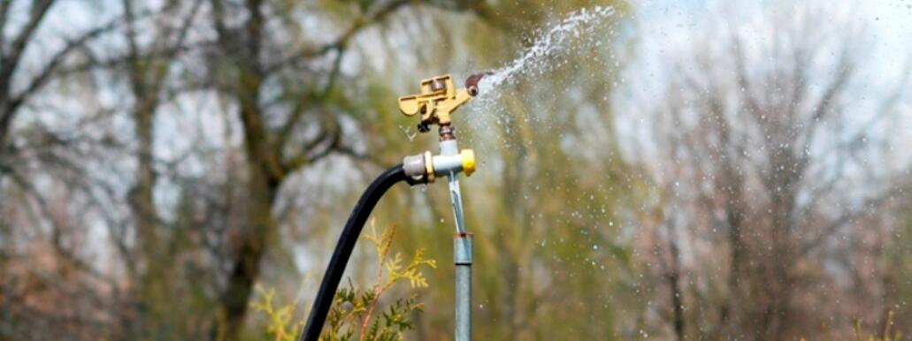 pipe in ground with hose attached and sprinkler head spraying water