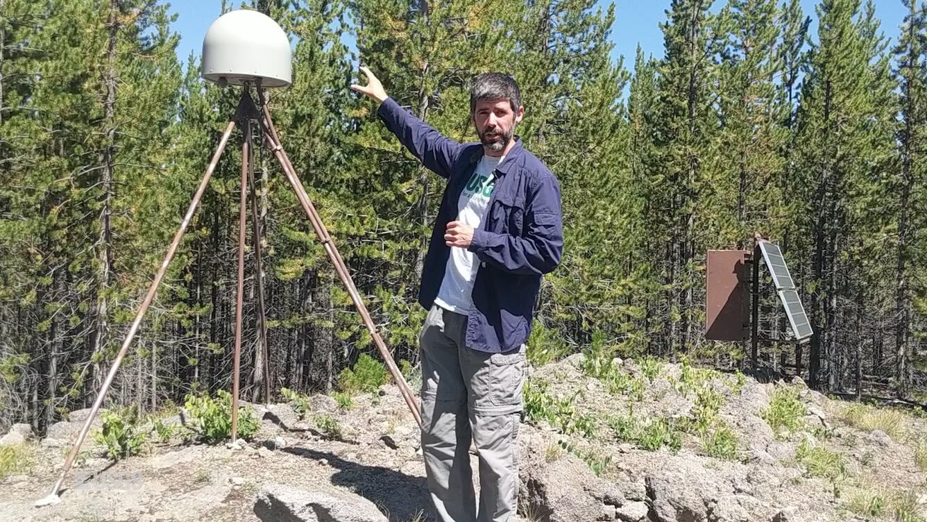 Man standing and pointing at scientific equipment in the background.
