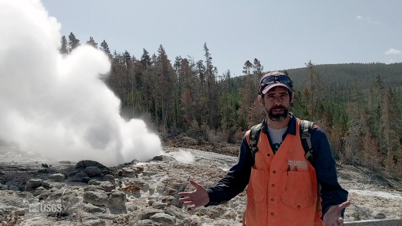 Man standing in front of a geyser with orange vest on