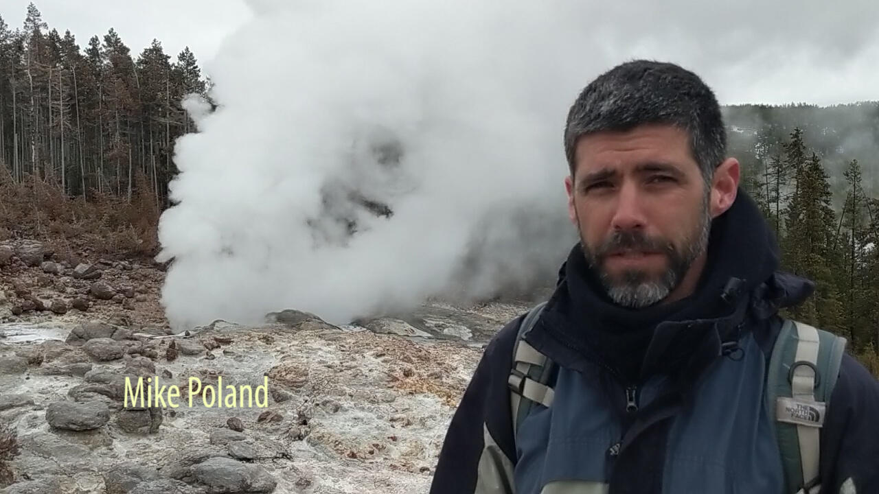 Man standing in front of a geyser releasing steam