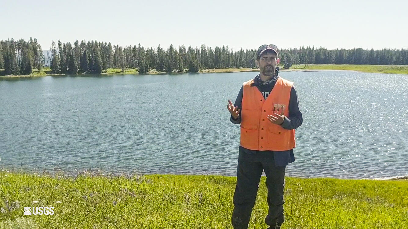 Man standing in front of a lake with orange vest on