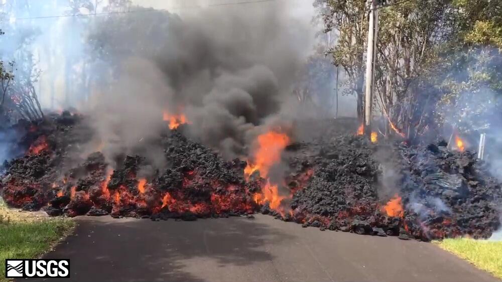 large lava flow rolling over road and through trees