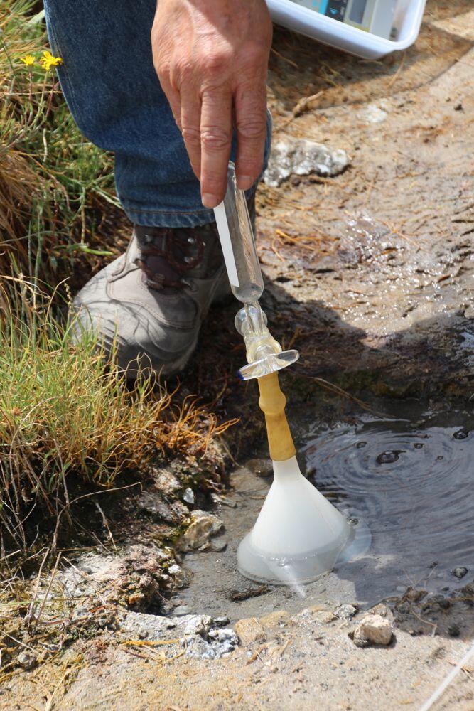 Volcanic gas collection via a funnel resting over bubbling spring -...