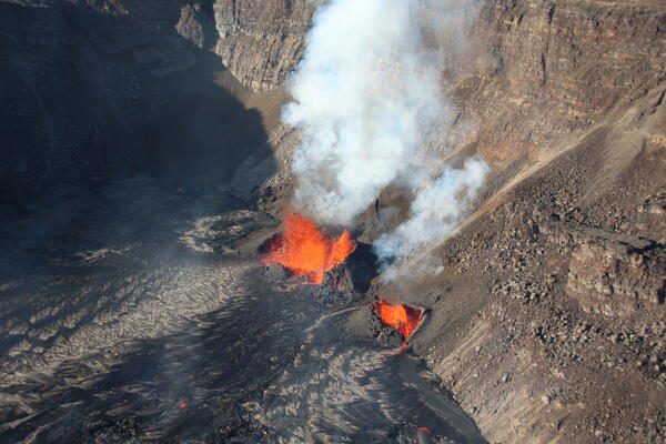 Orange incandescent lava fountains erupting from black lava on crater floor