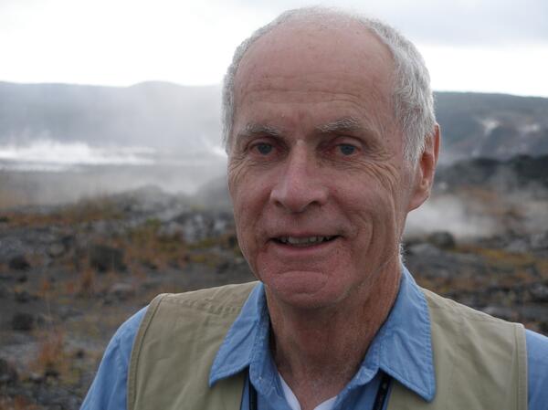 Color photograph of male scientist with steaming volcanic landscape in the background