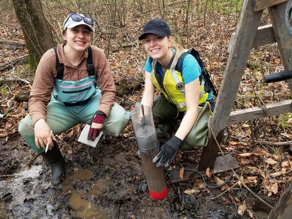 Two people crouched down in wetland smiling at camera working with equipment