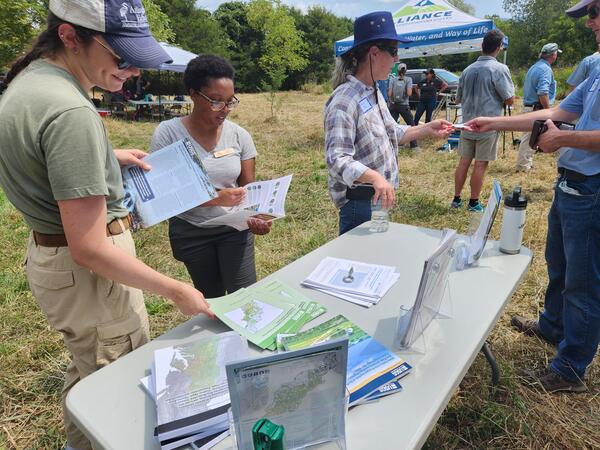 Community members gather at an outreach table, reading USGS fact sheets
