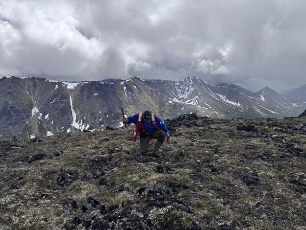 A man kneeling and holding a hammer on an alpine ridge.