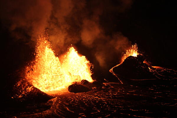 low-light photo of orange lava fountains erupting within a black spatter cone