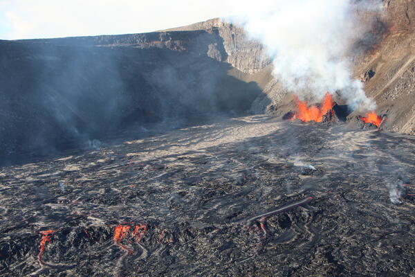 orange lava fountains erupting from the base of a crater wall
