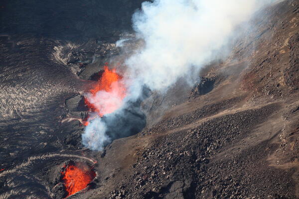Orange lava fountains erupting in black lava spatter cones with white gas plume being emitted