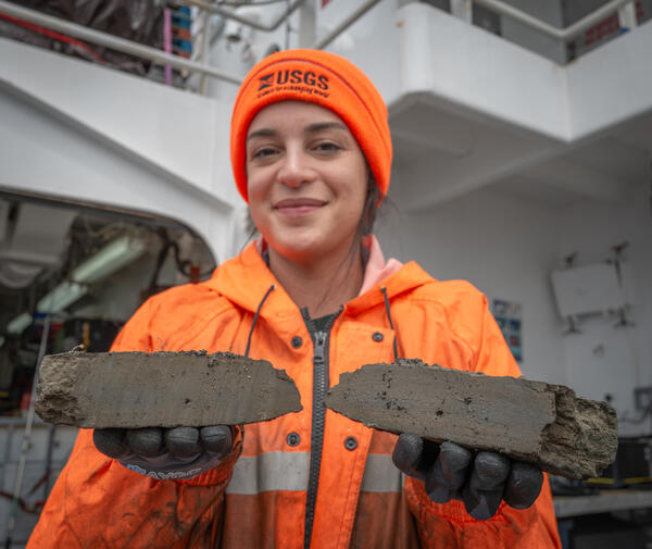 A person in an orange hat and jacket smiles towards the camera while holding rocks