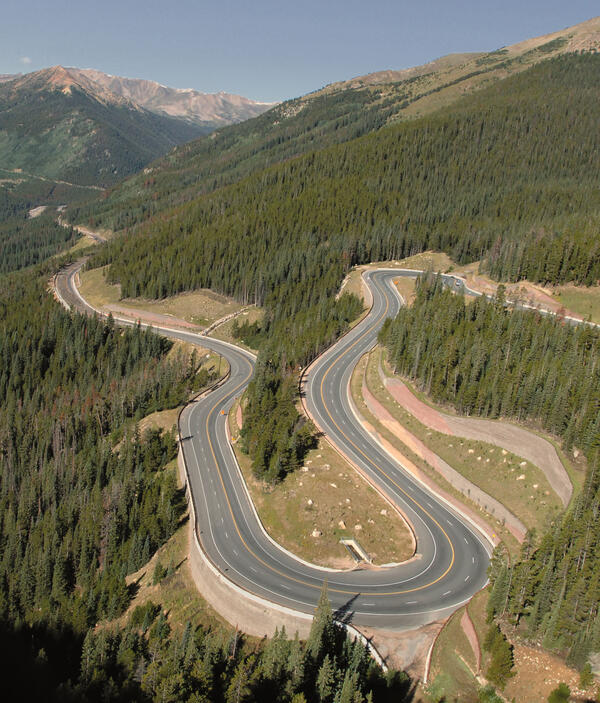 a road winds through forested, mountain terrain