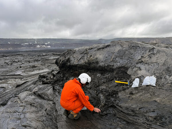 A scientist picking up pieces of lava from a lava flow surface