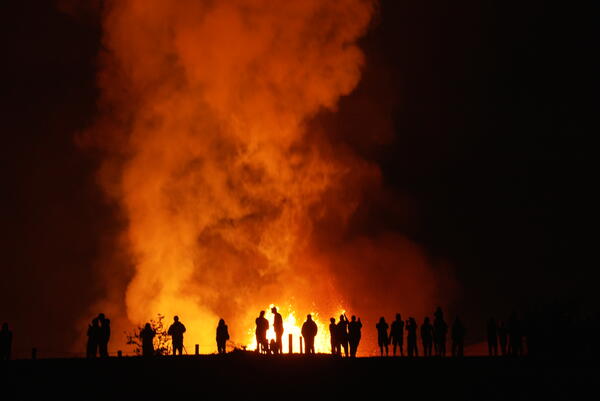 Silhouettes of people at night with a lava fountain and plume behind them