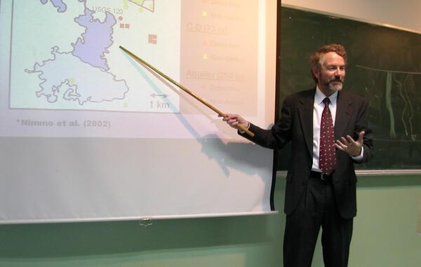 man lecturing in front of a projected image of a map 