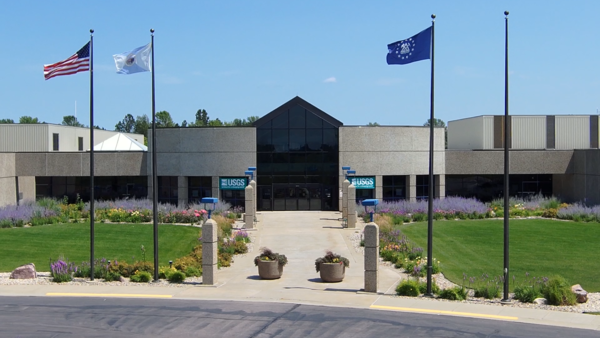 Entrance of building, with lawn, sidewalk, flagpoles and flowerpots