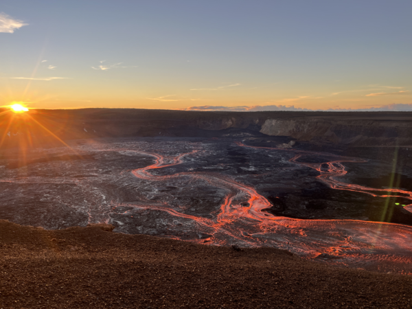 Color photograph of lava flowing in volcanic crater at sunrise