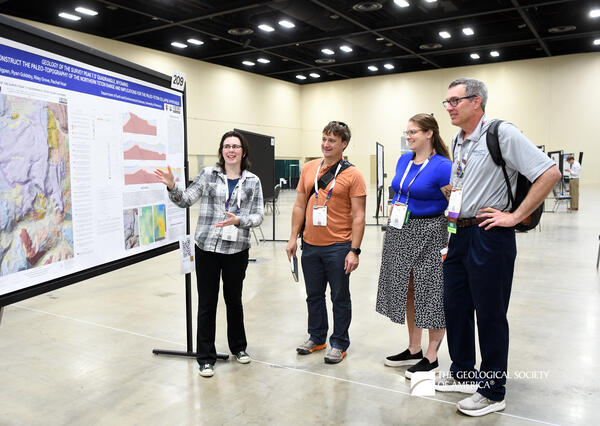 Four people standing to the right side of a geologic map poster. The person closest to the poster is gesturing towards it as they present the information.