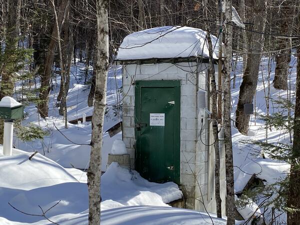 A streamgage house in a snowy, forested landscape.