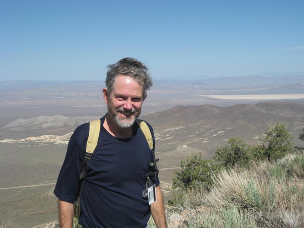 Man standing on a hill wearing a backpack with a view of sky and clouds in the background