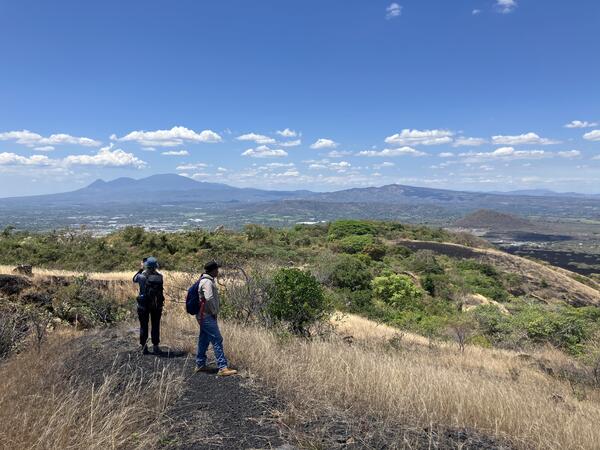 Color photograph of two people overlooking a volcanic landscape on a sunny day
