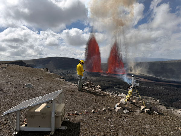 Two lava fountains erupt from vents on crater floor as scientist monitors in the foreground