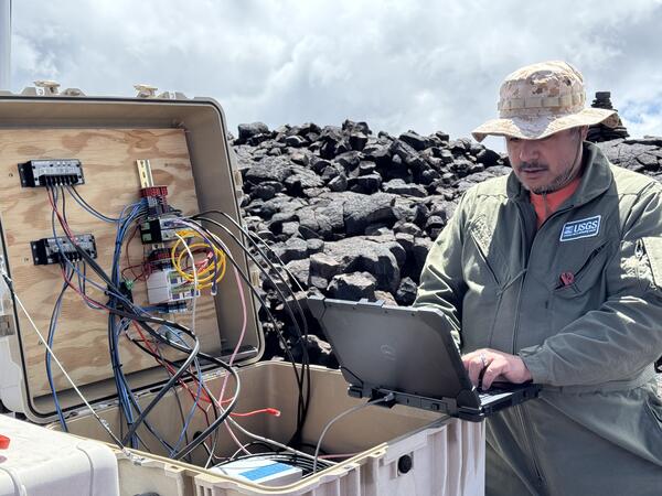 Color photograph of field engineer servicing a remote volcano monitoring site