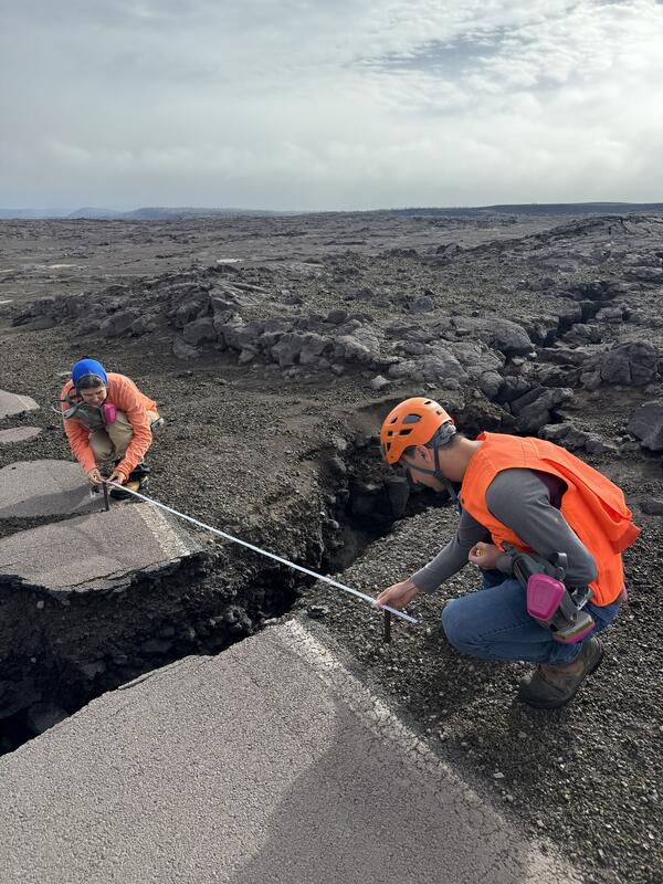 Color photograph of two scientists measuring a crack in a road