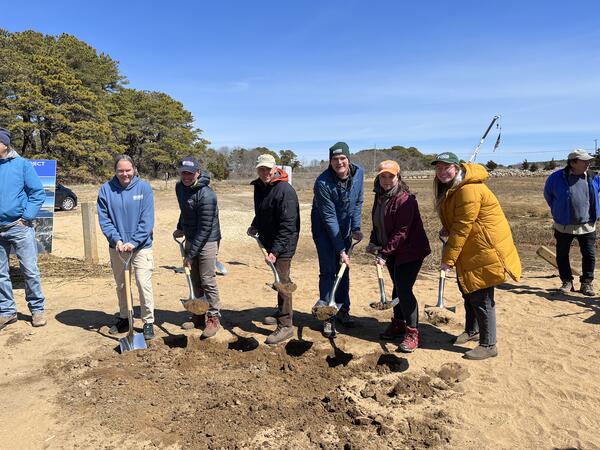 Six people outside digging ceremoniously and smiling