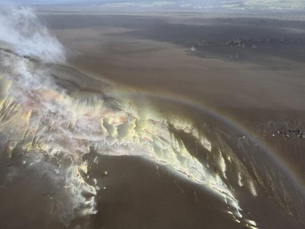 Color photograph of sulfur deposits on crater rim, with rainbow