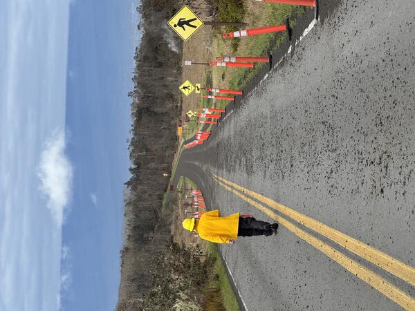 Color photograph of geologist walking road covered with volcanic fallout