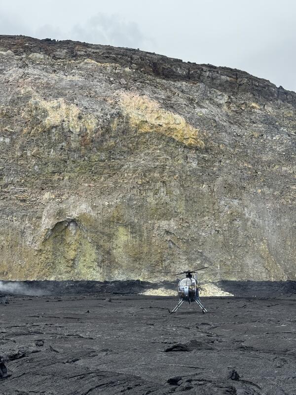 Color photograph of helicopter on crater floor with crater wall in background