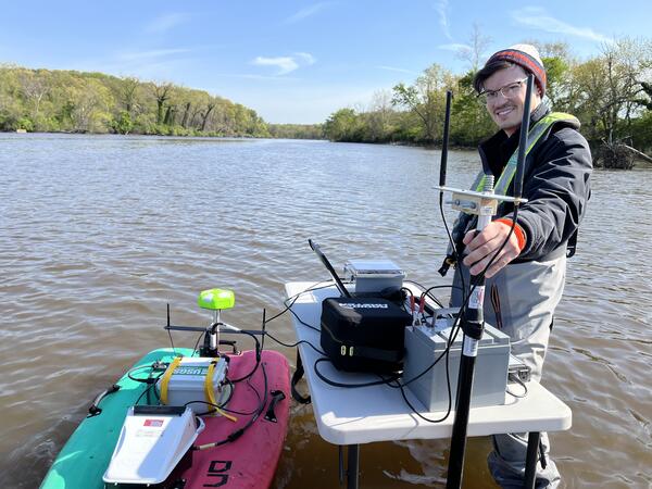 A hydrologic technician poses with an autonomous miniature boat in the Anacostia River.