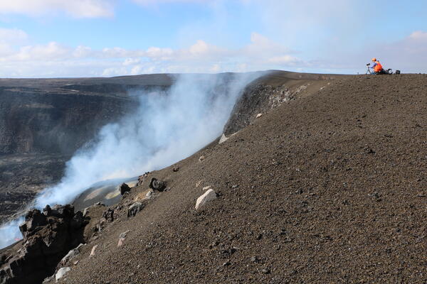 Color photograph of scientist checking monitoring equipment on the rim of a crater