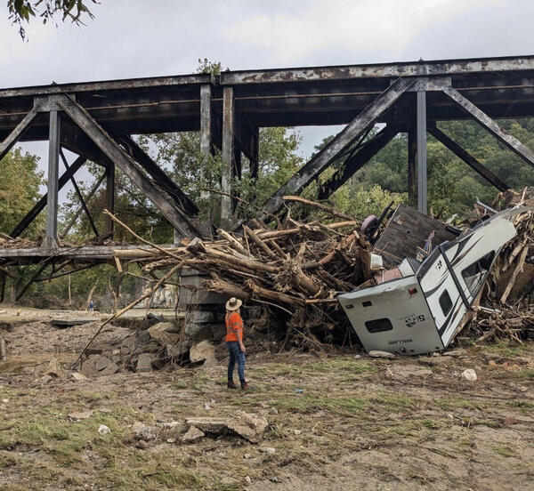 Image shows a large pile of debris left behind after major flooding. A damaged camper can be seen in the pile. 