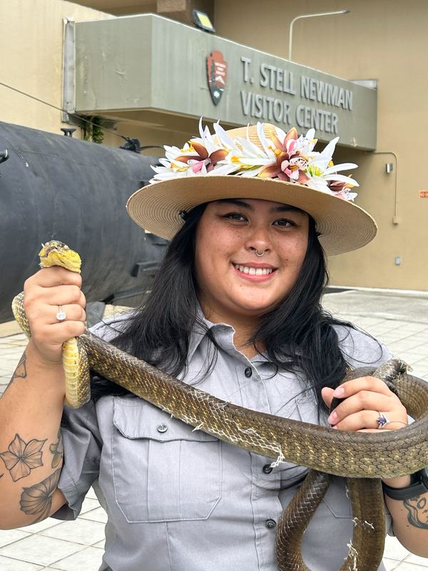 park worker with hat stands in front of building holding snake 