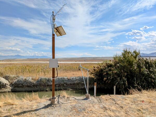 Narrow, small desert canal-like stream surrounded by dried grass with valley background.