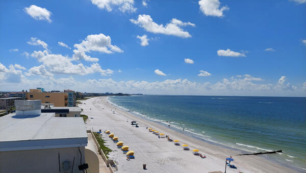 A view taken from a roof of a long white beach, yellow umbrellas on the beach, and a calm blue ocean in FL