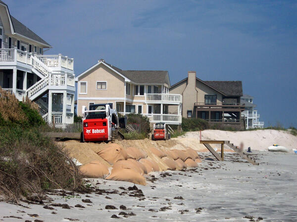 Make-shift seawall sandbags support an eroded dune below coastal homes on the beach