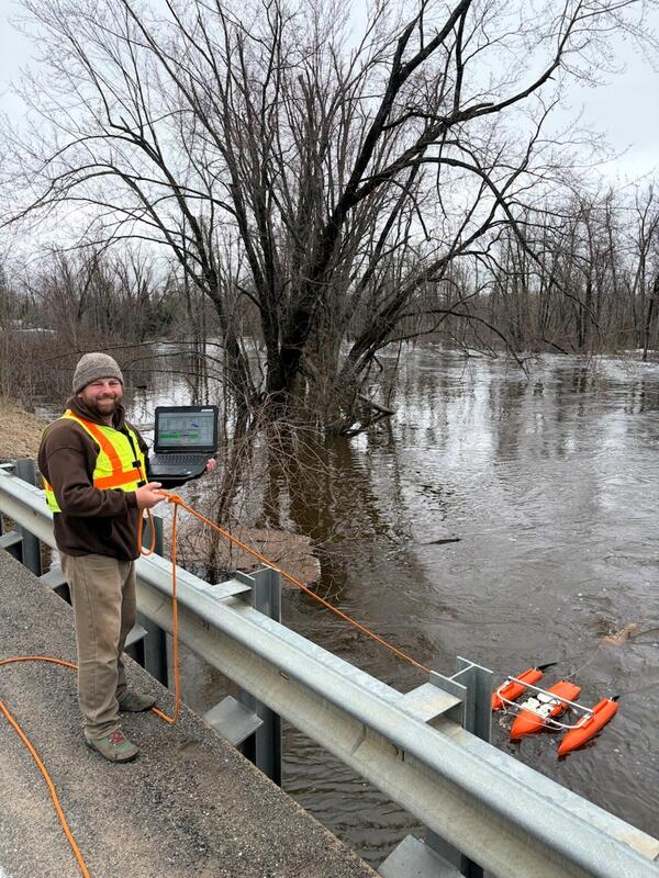 Hydrologic technician measures streamflow off bridge using ADCP on flooded river