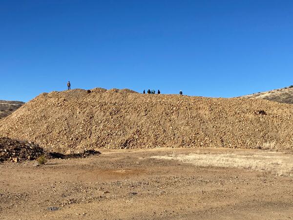 A pile of brown rocks, waste left after hard-rock mining, and behind it, blue sky.