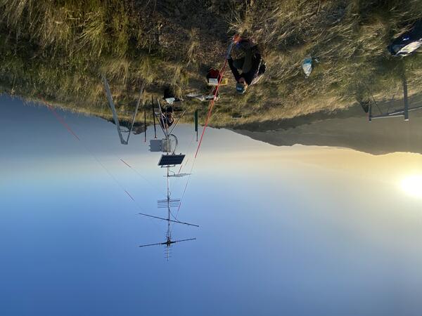 USGS scientists install a remote Motus Wildlife Tracking System on Santa Catalina Island off southern California. The USGS scientist is seen installing the Motus Station on the grass covered Feltcher Peak that overlooks mountain and water, seen in the background.